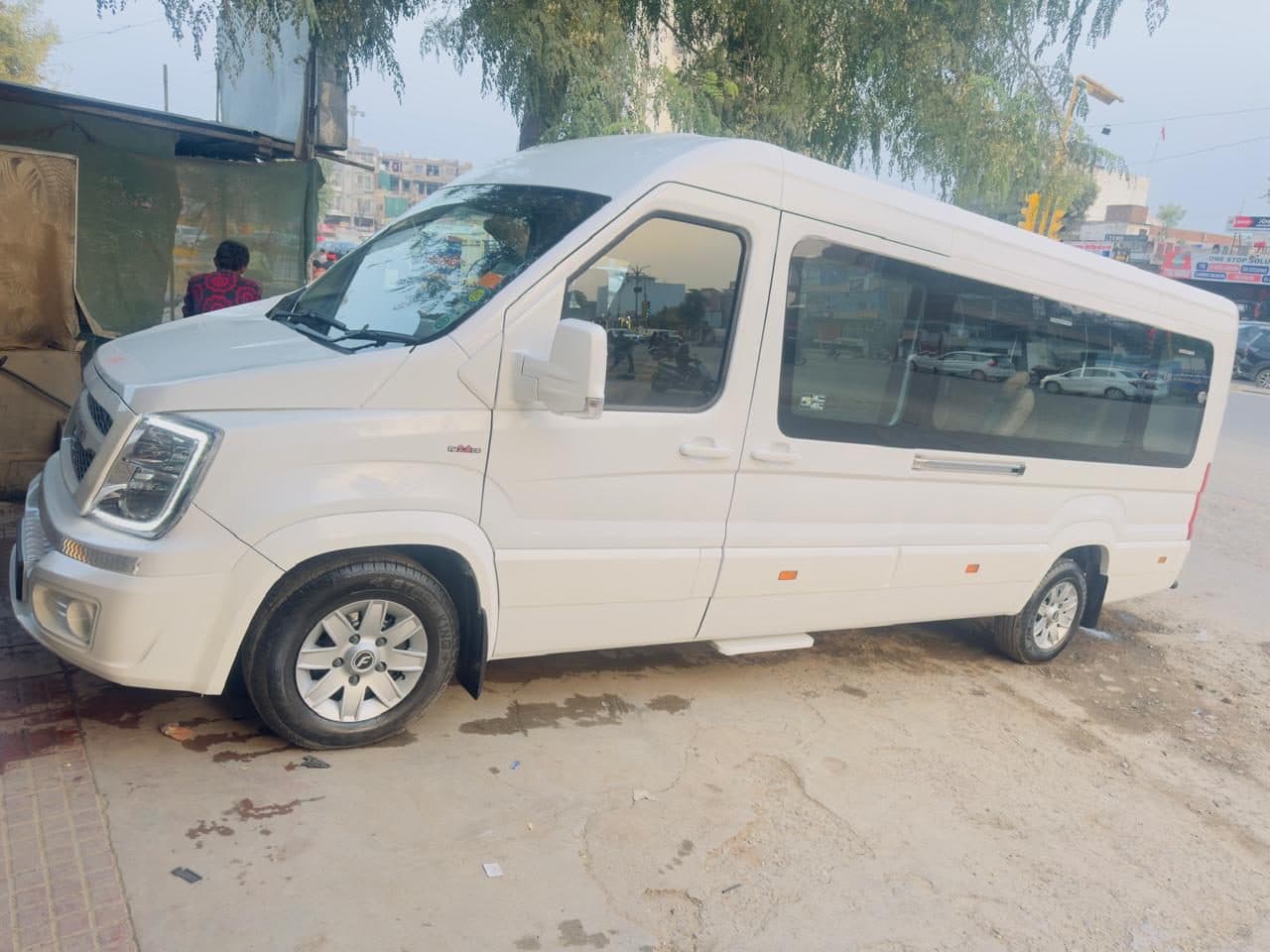 A white air-conditioned tempo traveller coach parked under trees, waiting
