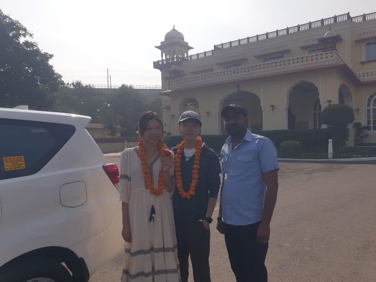 A couple in red garlands with their guide arriving by SUV at the gate of a Rajasthan palace hotel