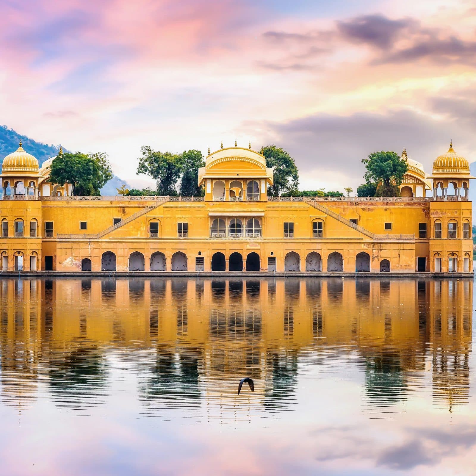The Jal Mahal water palace sitting mid-lake in Jaipur under a pink dusk sky