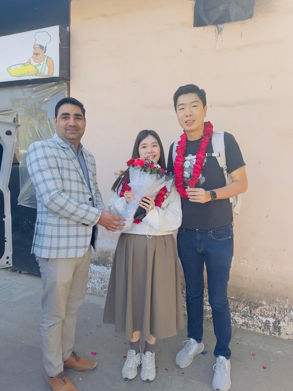 A guide handing a bouquet to two guests in fresh flower garlands outside the airport terminal