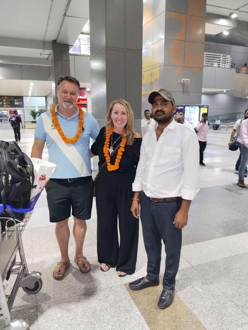 A guide and a couple in garlands posing for a photo at the arrivals kerb