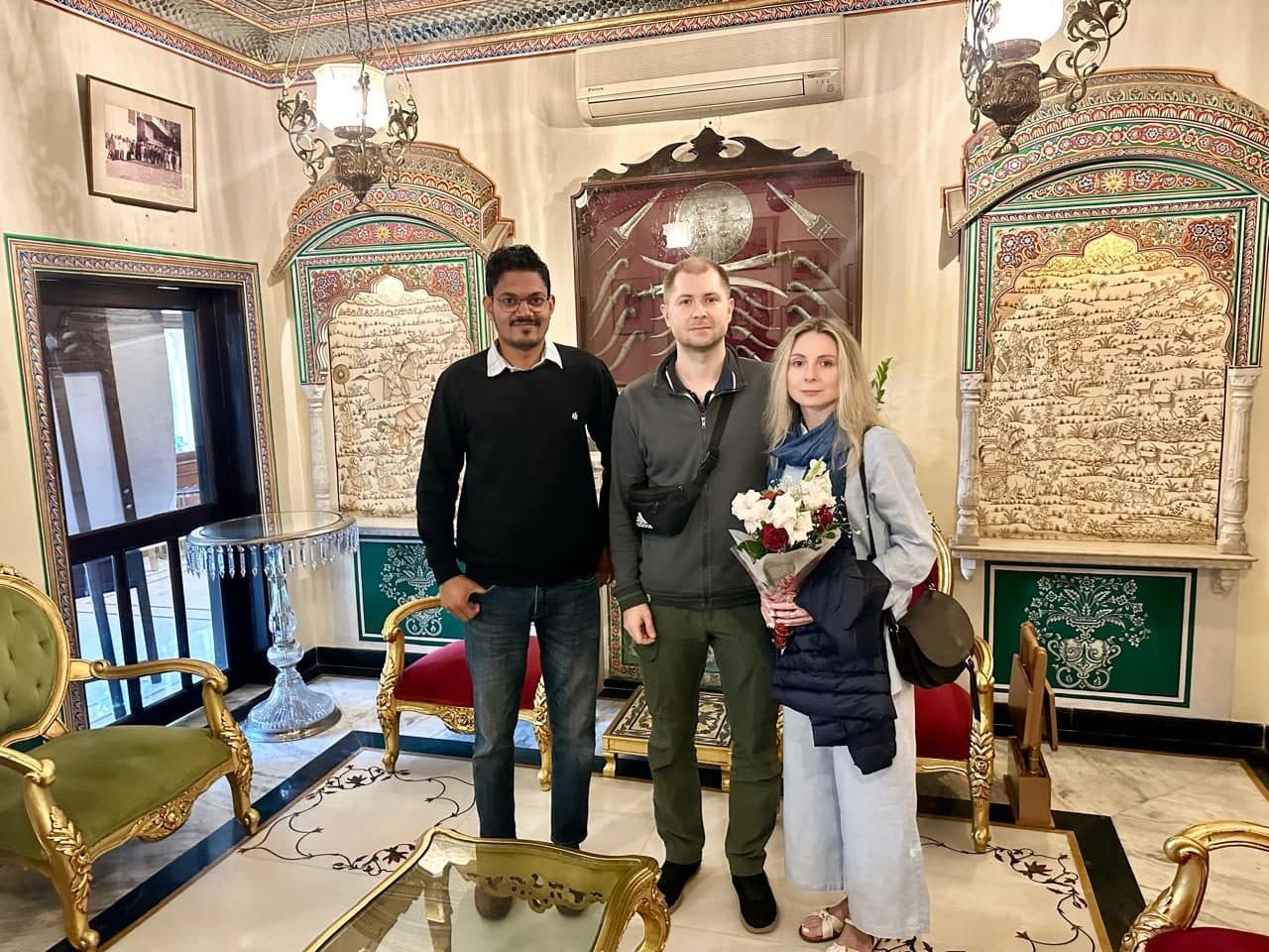 Three people standing in a gilded, fresco-painted drawing room of a heritage haveli
