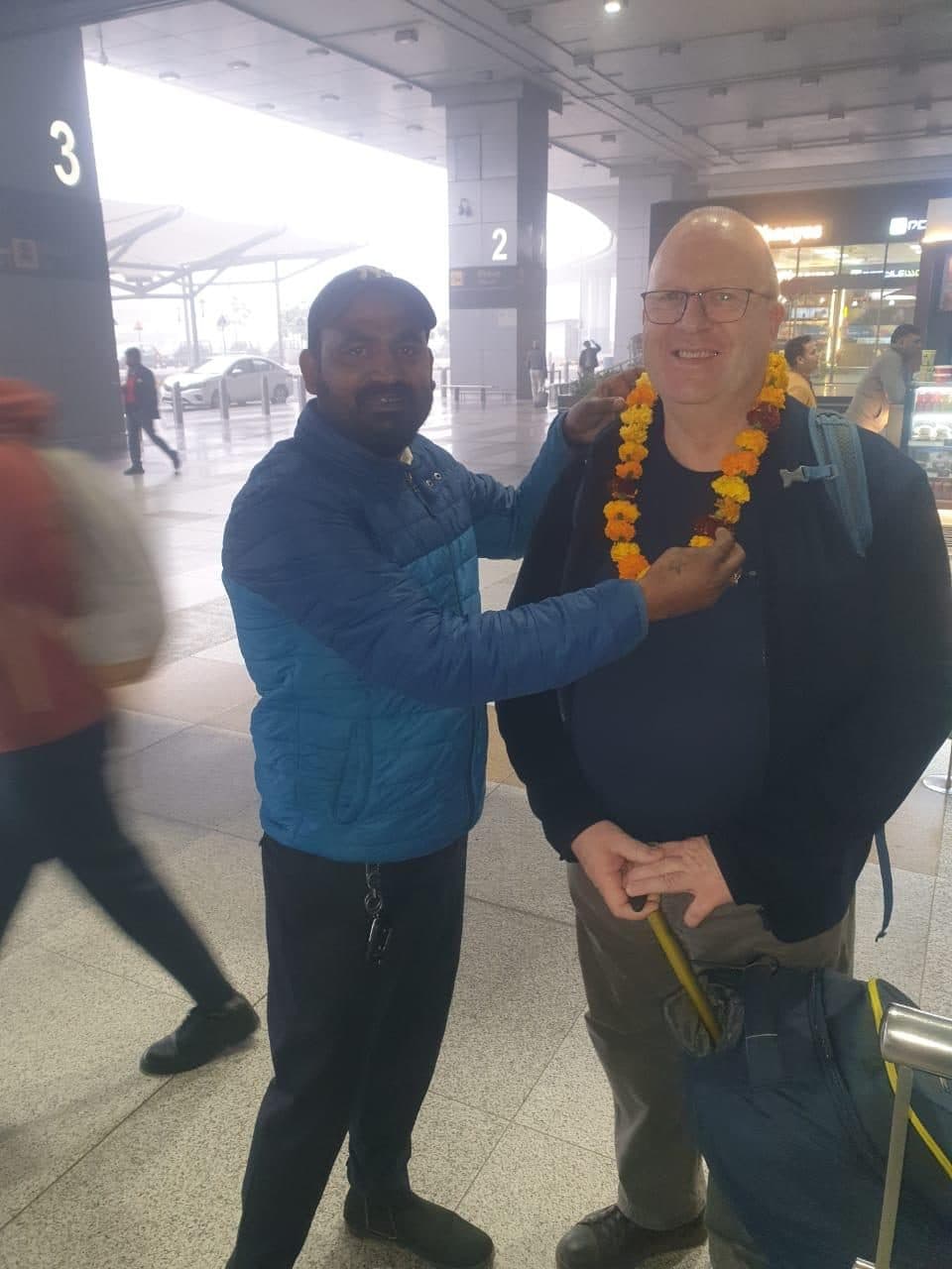 A guide greeting a garlanded guest with a warm handshake on the terminal forecourt