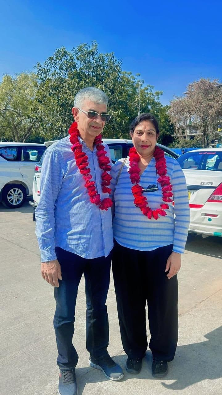 A couple in red rose garlands waiting for their transfer, the fleet cars lined up behind