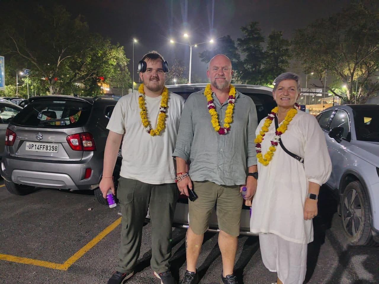 A group of four guests, all in marigold garlands, in a car park at night