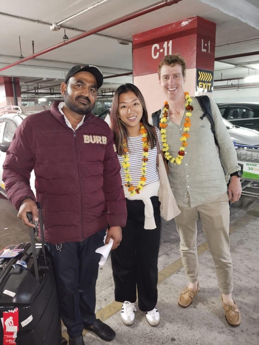 A guide in a maroon jacket with a couple in garlands in the arrivals car park