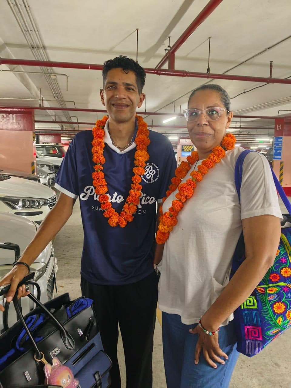An older couple in marigold garlands welcomed by their guide on the lower-ground pickup level