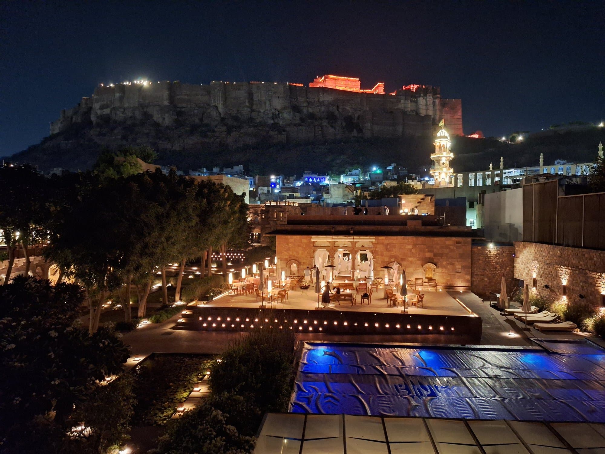 RAAS Jodhpur's pool terrace at night, candlelit with Mehrangarh Fort floodlit red on the hilltop behind
