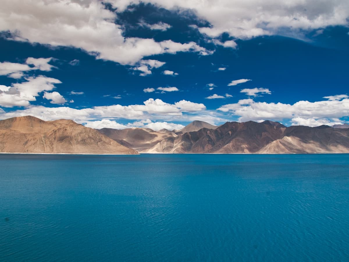 The shifting blue and teal water of Pangong Tso against brown and snow-streaked mountains, a 134-kilometre lake straddling Ladakh and Tibet.