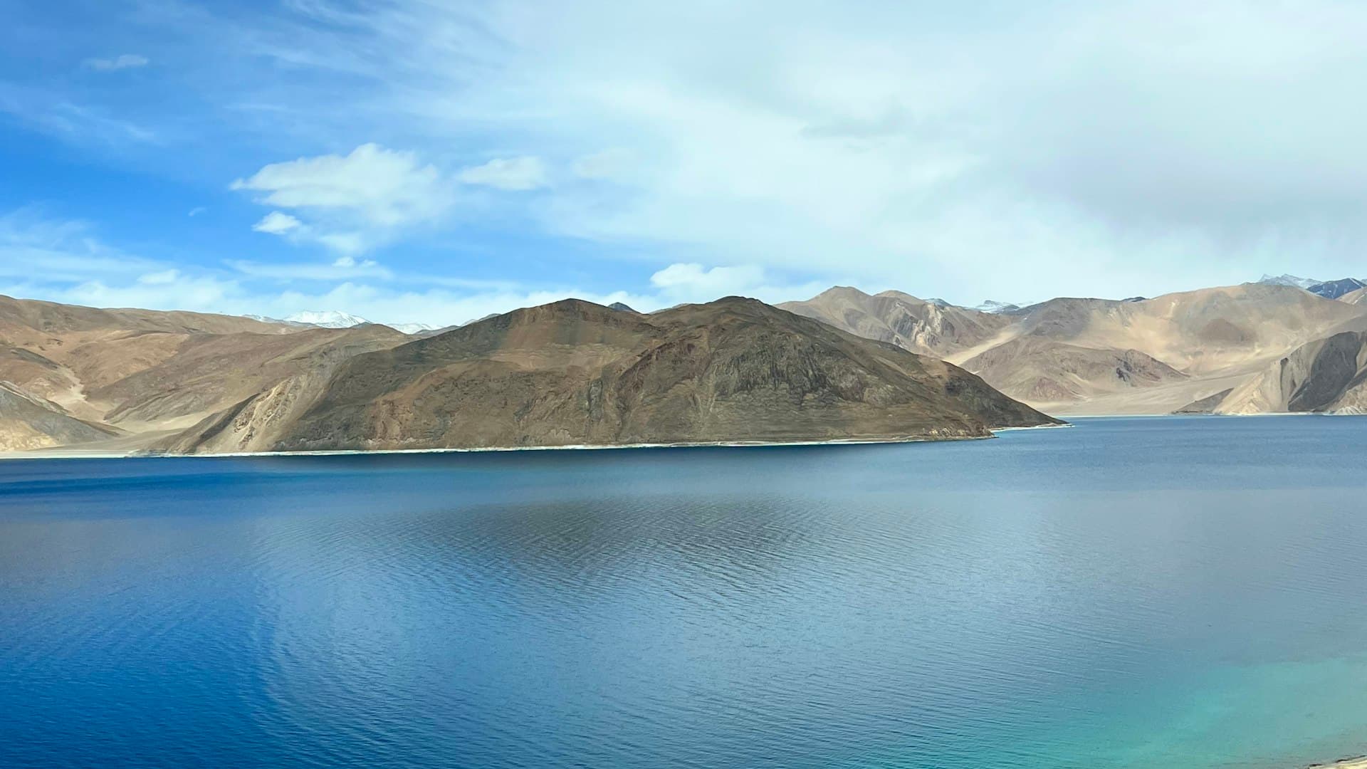 The blue expanse of Pangong Lake in Ladakh with layered hills and snow peaks along the far shore under a clear sky