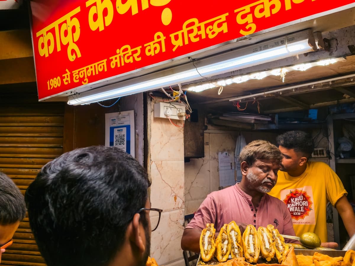 A vendor lifts fried snacks from a metal tray at a busy Old Delhi street-food stall near Connaught Place.