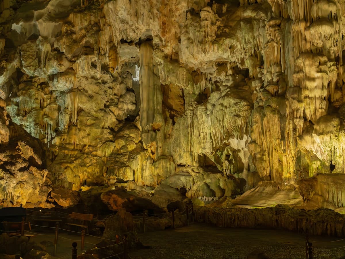 A lit limestone cave passage with stalactite and stalagmite formations.