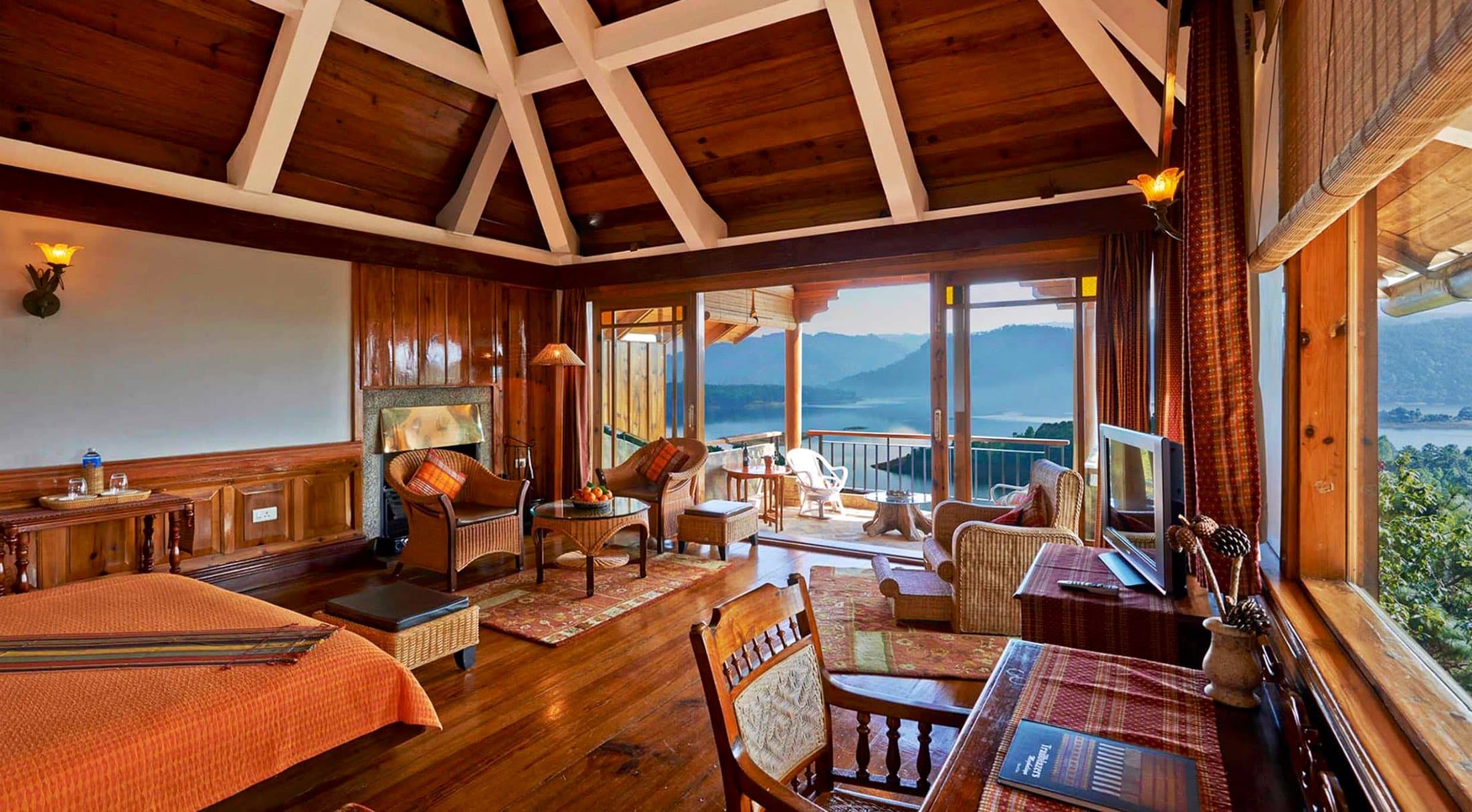 An open-sided timber lounge and dining pavilion at Ri Kynjai framing a view of Umiam Lake.