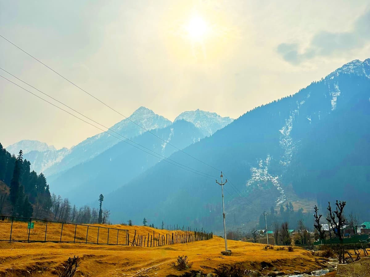 A stream winds through an alpine meadow ringed by mountains in Aru Valley near Pahalgam.