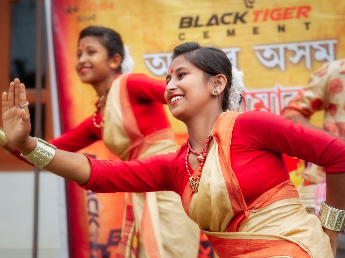 Two women in traditional Assamese attire perform a dance.