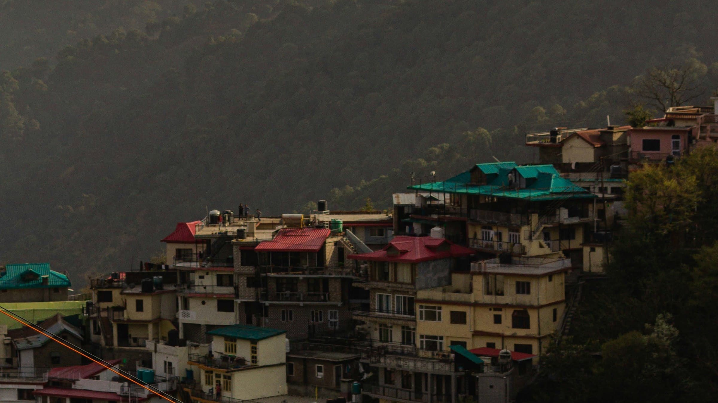Aerial view of the cantonment hill town of Kasauli with cottages on a forested slope and Himalayan foothills behind, Himachal Pradesh.