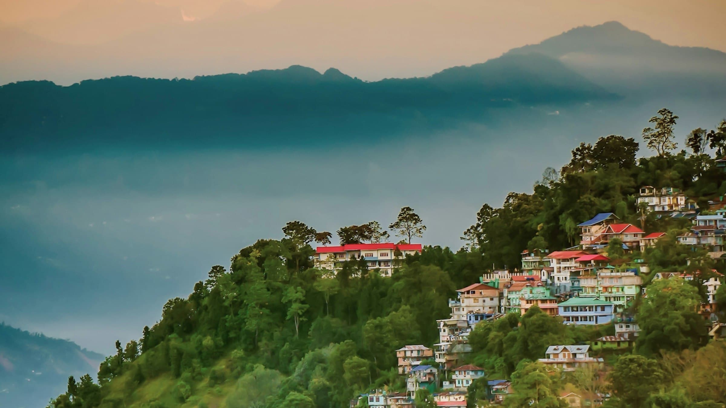Kalimpong hill town on a green mountain slope with the Himalayas rising behind it, West Bengal