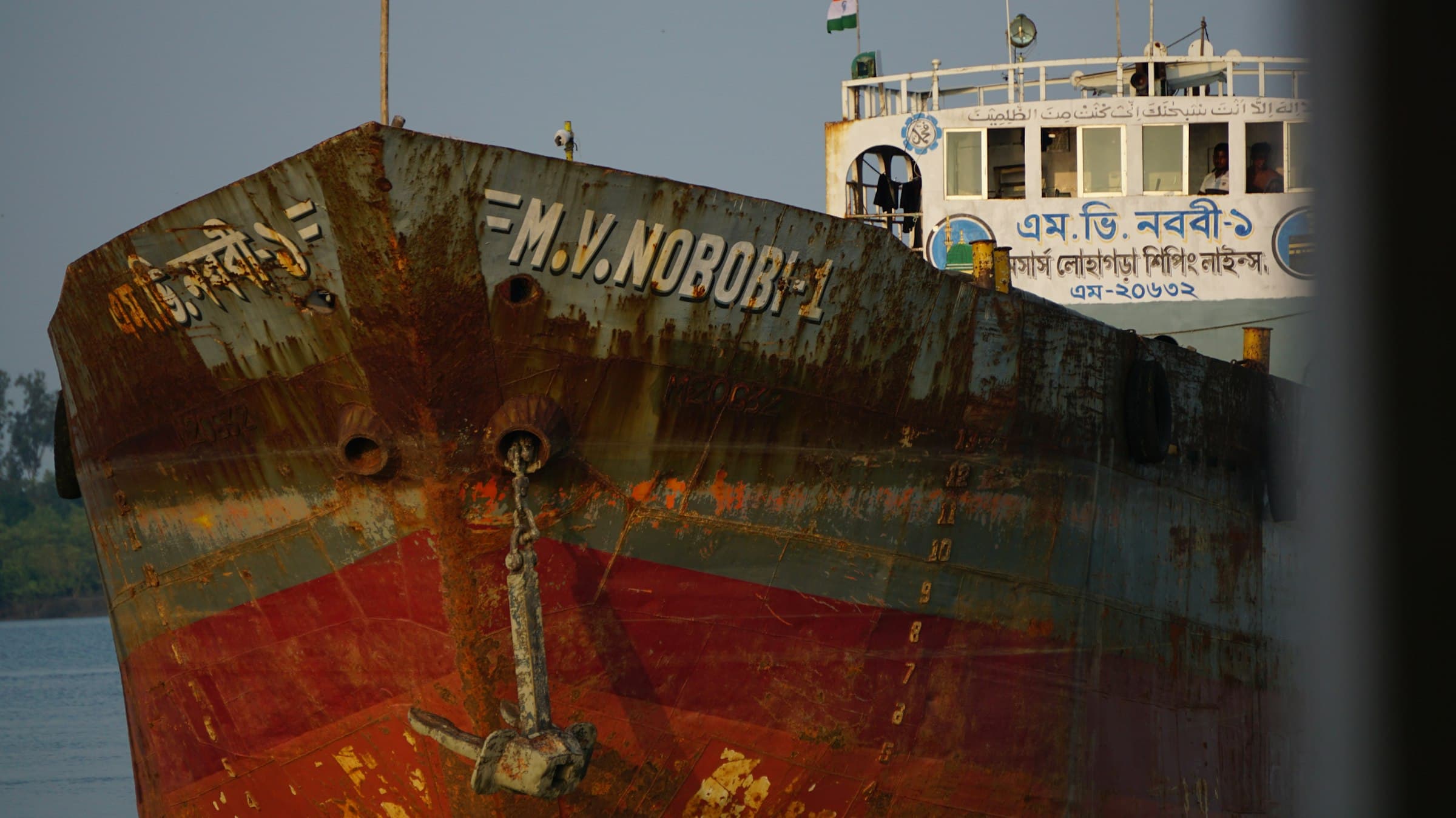 A rusted cargo vessel gliding through a tidal waterway in the Sundarbans mangrove delta, West Bengal