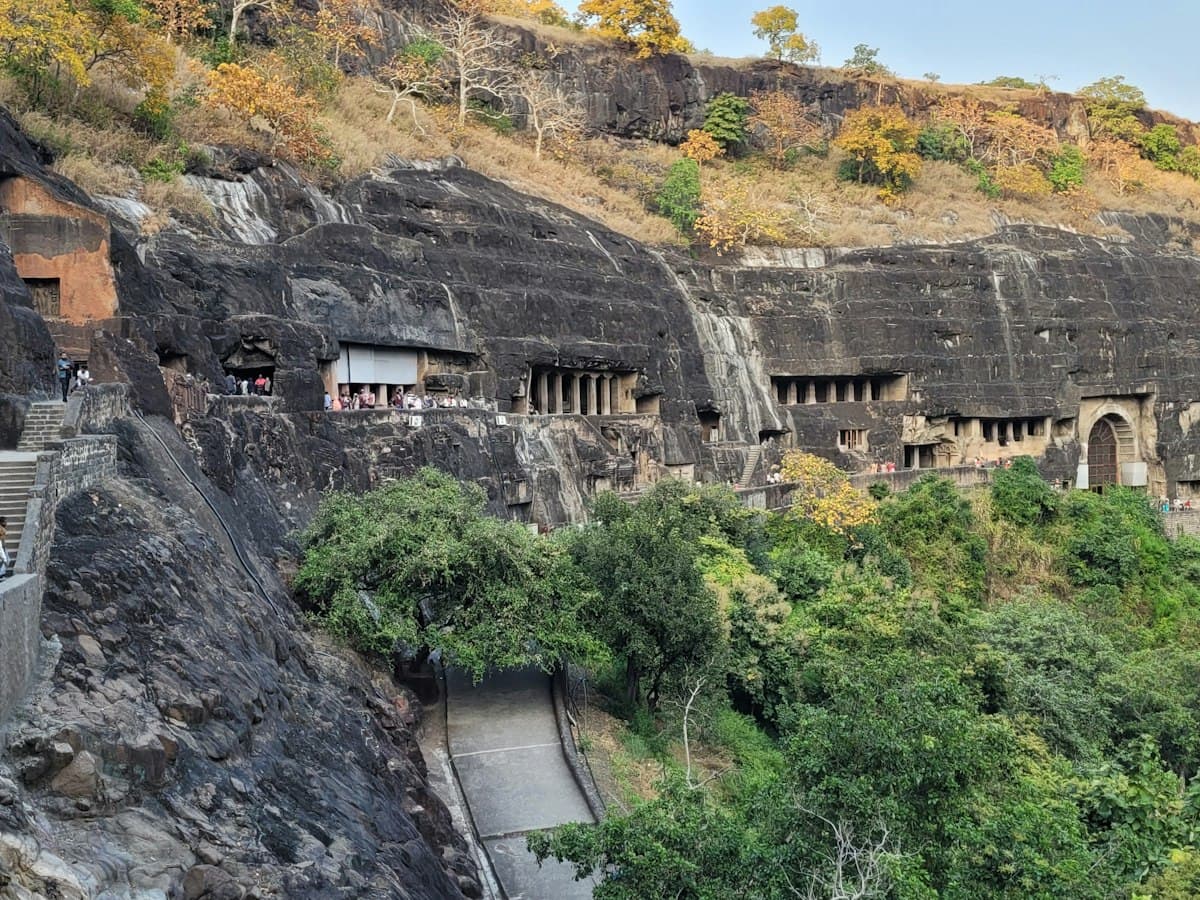 Ancient rock-cut caves carved into a green hillside at Ajanta, Maharashtra