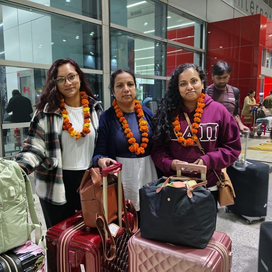 Three guests wearing marigold garlands with their luggage at the airport on arrival