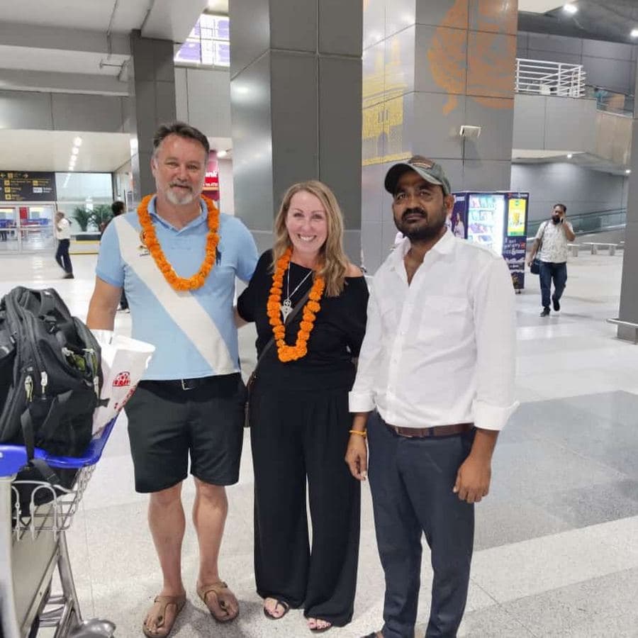 Three guests wearing marigold garlands at the airport, greeted by their tour guide