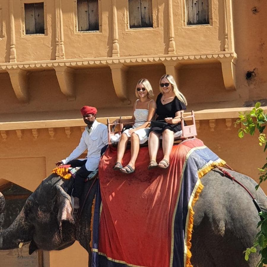 Two guests riding a decorated elephant with its mahout up to Amber Fort