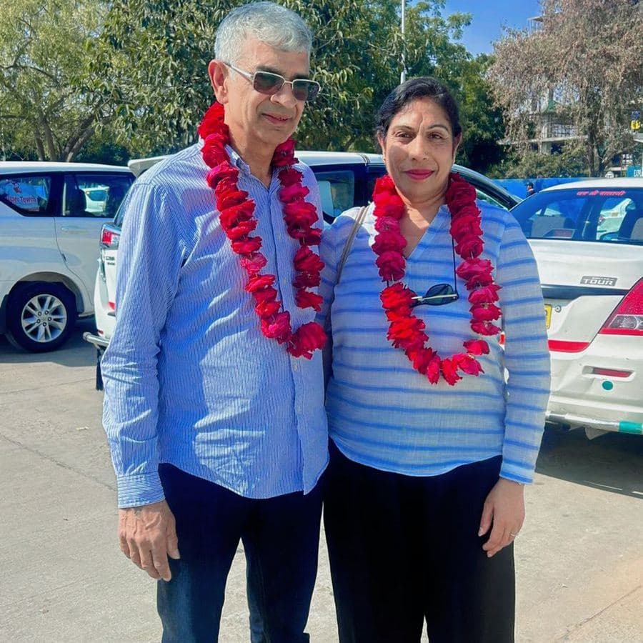 A couple wearing red flower garlands, welcomed roadside beside their private car