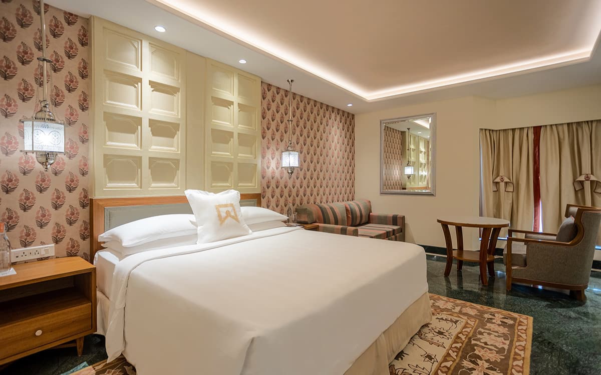 A Mughal Chamber room at ITC Mughal Agra with a patterned headboard and dark wood furnishings