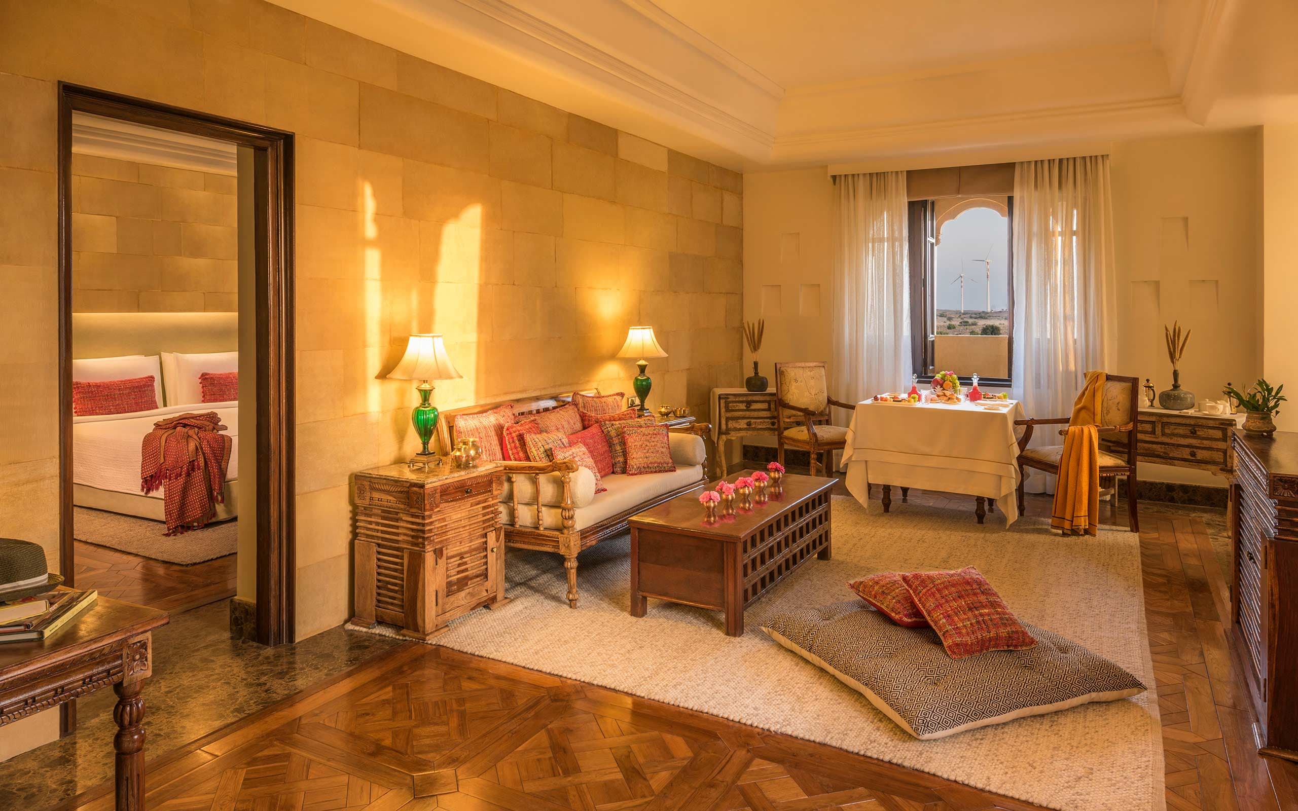 Sitting area of a Suryagarh suite with handcrafted wooden furniture, red block-print cushions, and a breakfast table by the window