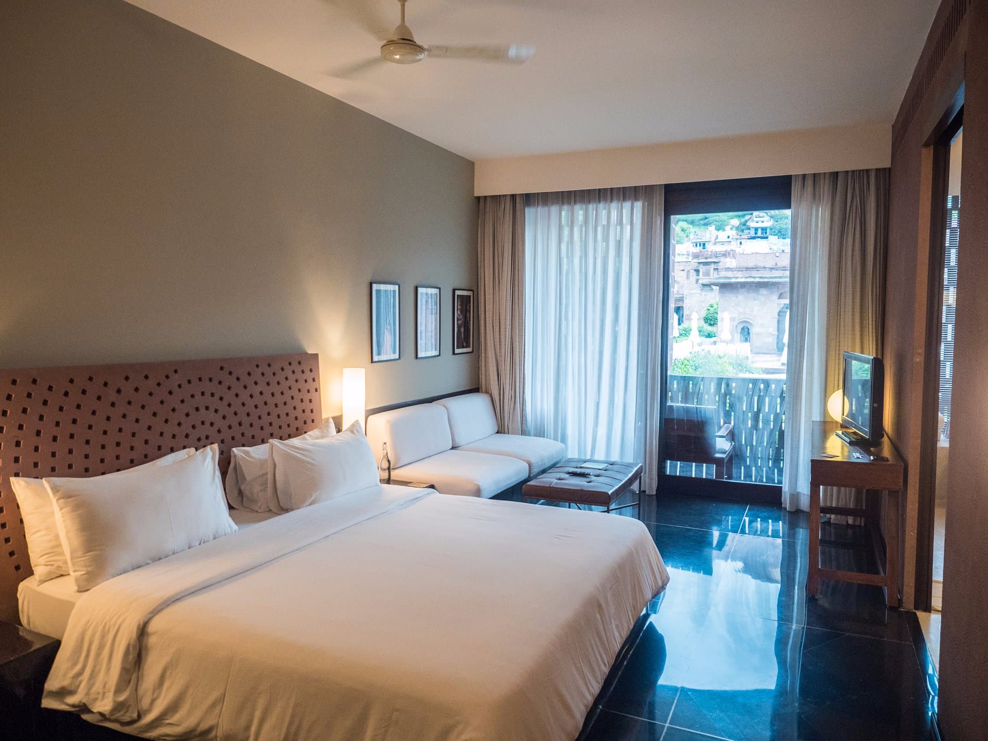 A RAAS Jodhpur Deluxe Room with a seating nook and a balcony overlooking the old city's sandstone rooftops