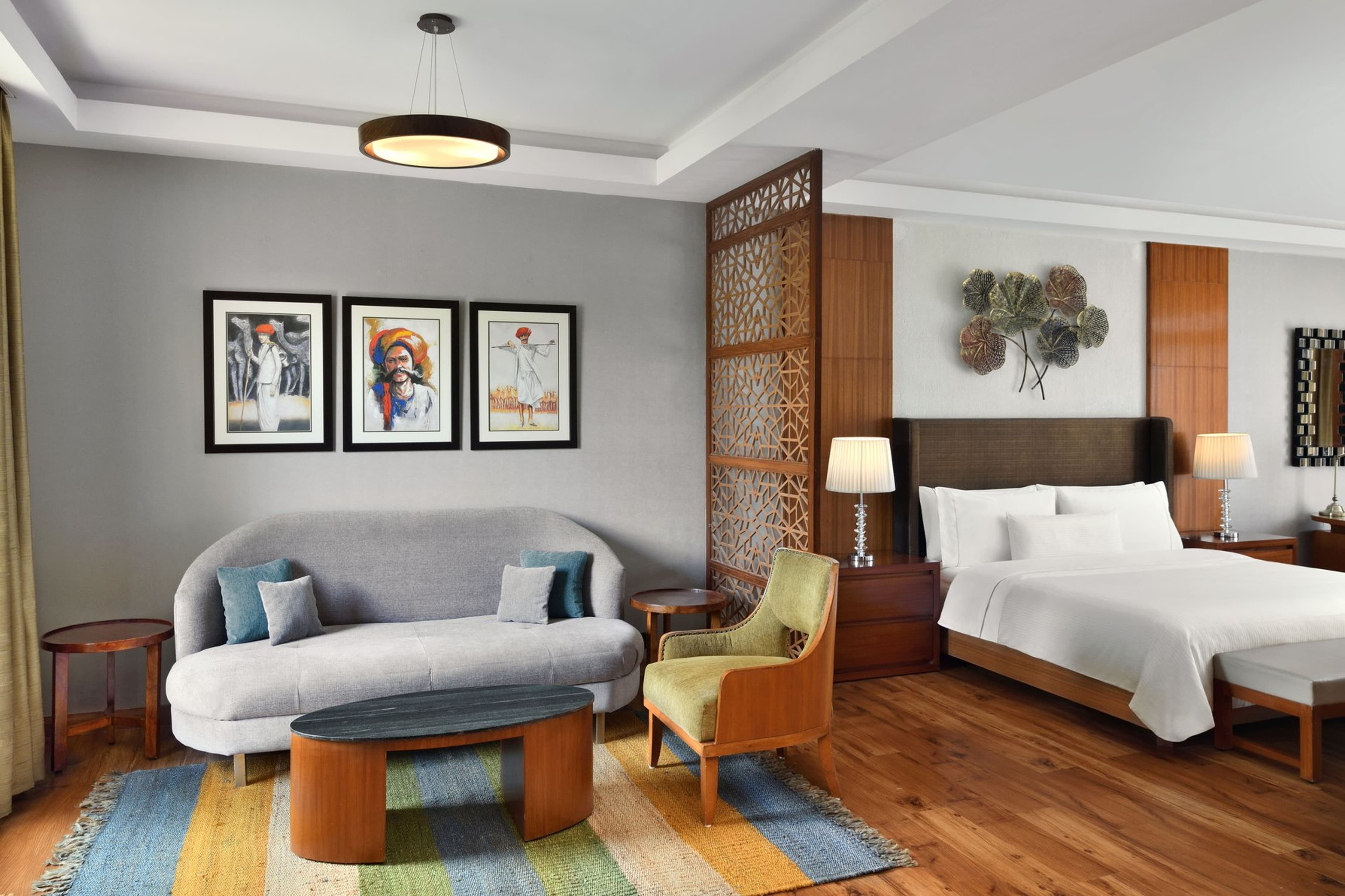 A Westin Pushkar Deluxe Garden View Room with king bed, Rajasthani portrait art, and a grey sofa seating area