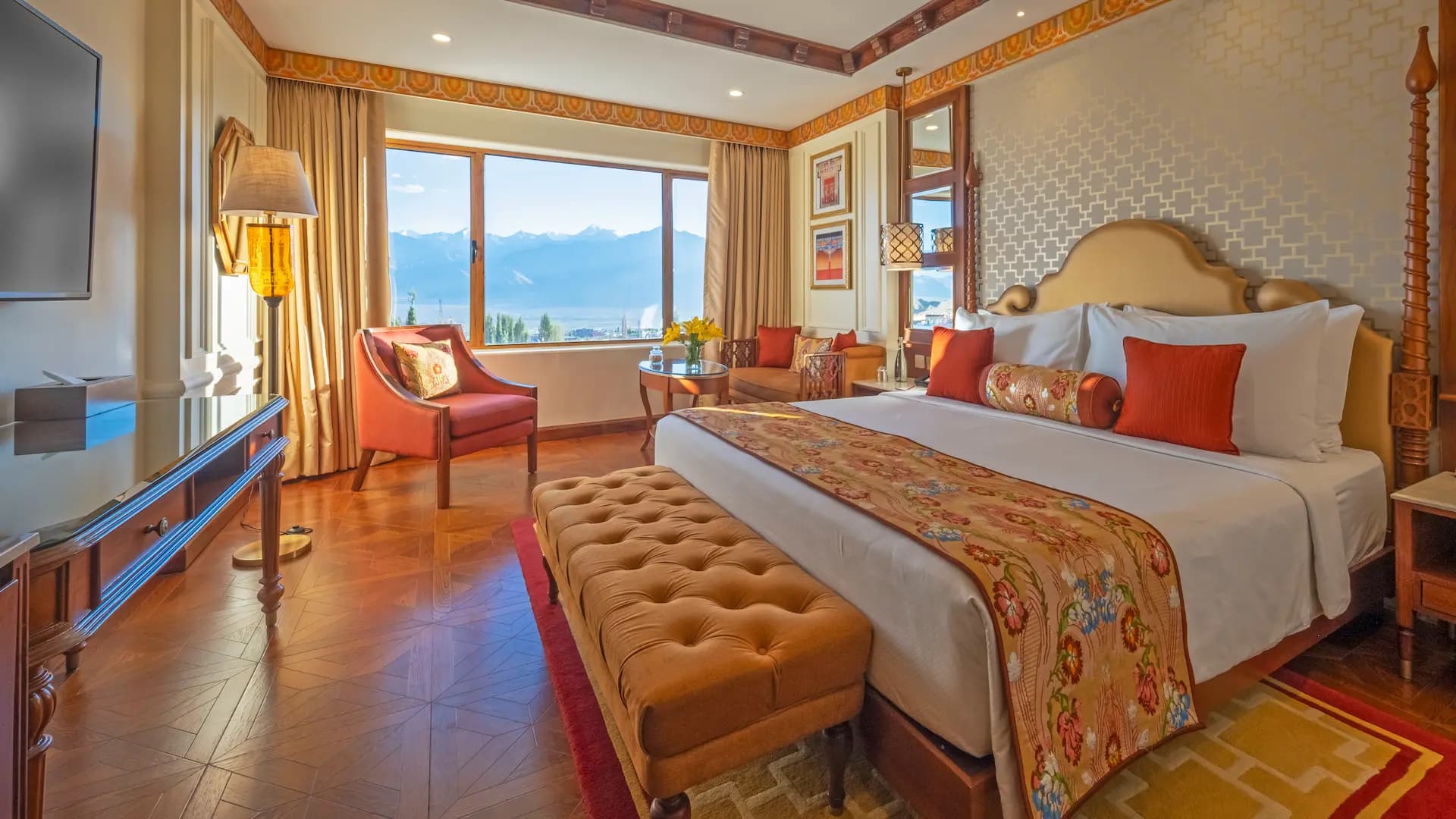 Luxury Room at The Grand Dragon Ladakh in Leh with a king bed, tufted ottoman and floor-to-ceiling windows framing a mountain and lake view