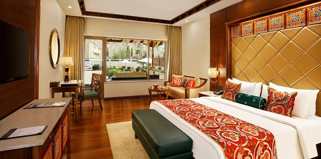 Premier Heritage Room at The Grand Dragon Ladakh with a carved padded headboard, warm wood floor and a window seat looking onto the courtyard