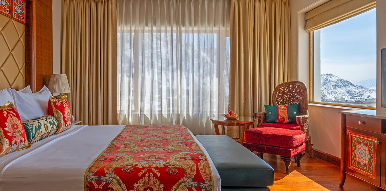 Family Suite bedroom at The Grand Dragon Ladakh with brocade bed runner and a picture window looking out to snow-capped Ladakh peaks