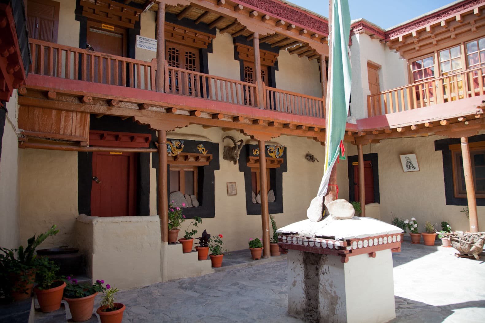 The inner courtyard of Stok Palace in Ladakh with timber balconies, painted dragon reliefs and potted flowers around a central chorten