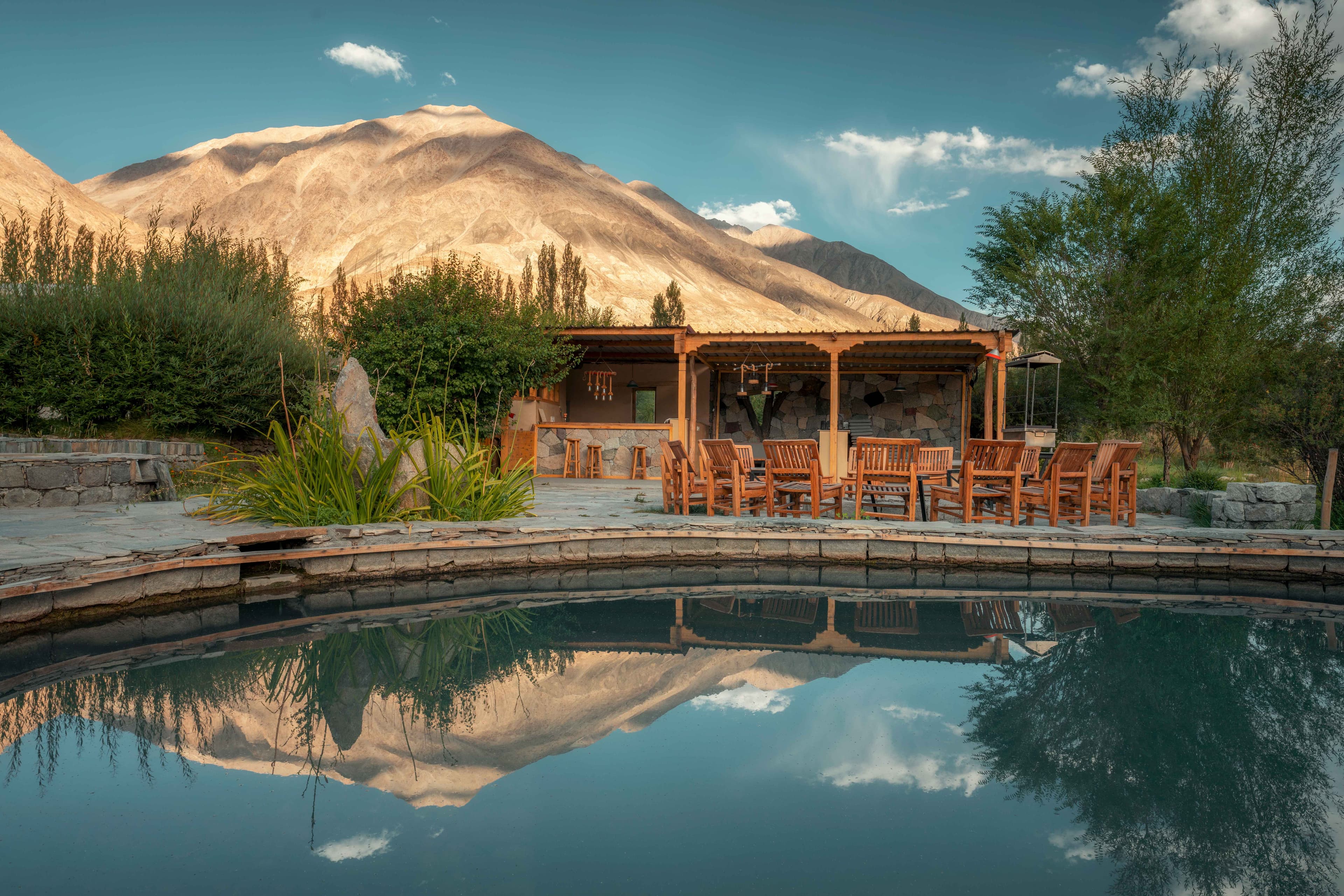 A timber-framed pavilion and reflecting pool in the gardens of Lchang Nang Retreat, mirroring the Nubra Valley mountains at dusk