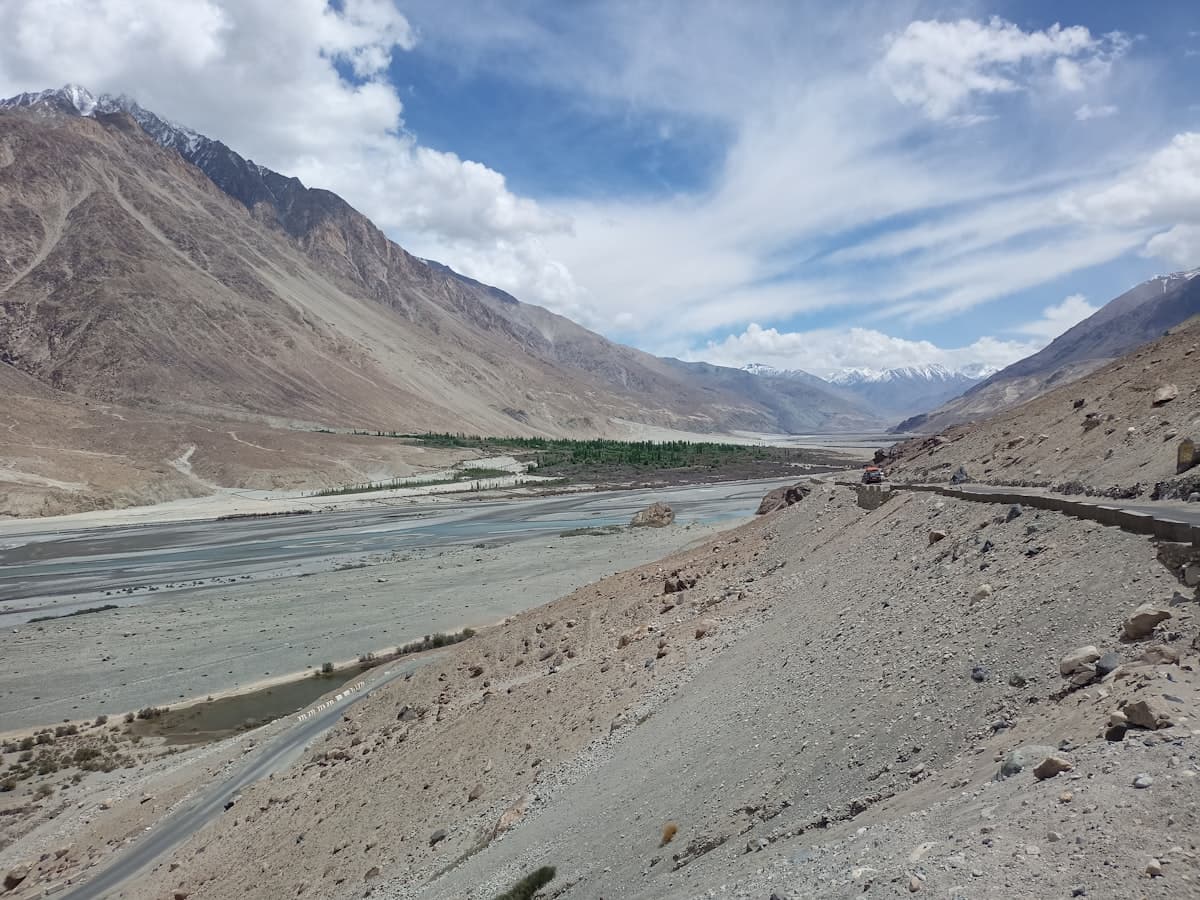 A wide grey river braids across the floor of the Nubra valley beneath steep, bare mountain walls on the rough road toward Pangong.