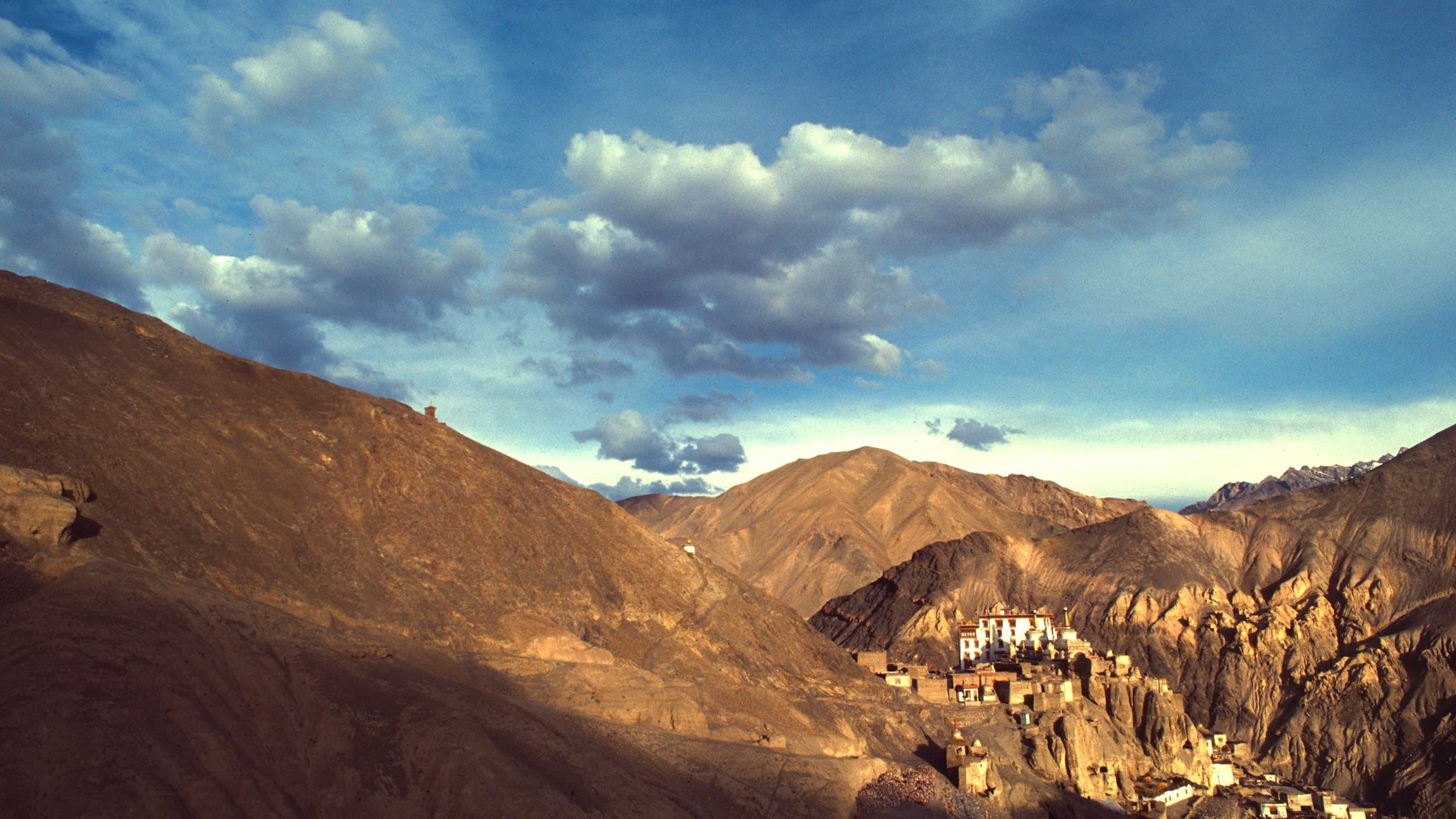 A cluster of village houses nestled on a valley floor beneath the bare, weathered brown mountains of western Ladakh, near Lamayuru.