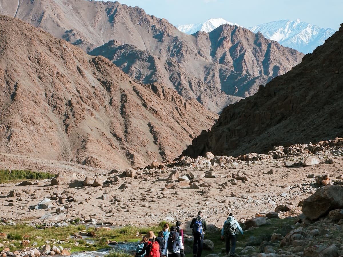 A small group of walkers climbs an open trail through the brown hills of Ladakh under a wide Himalayan sky.