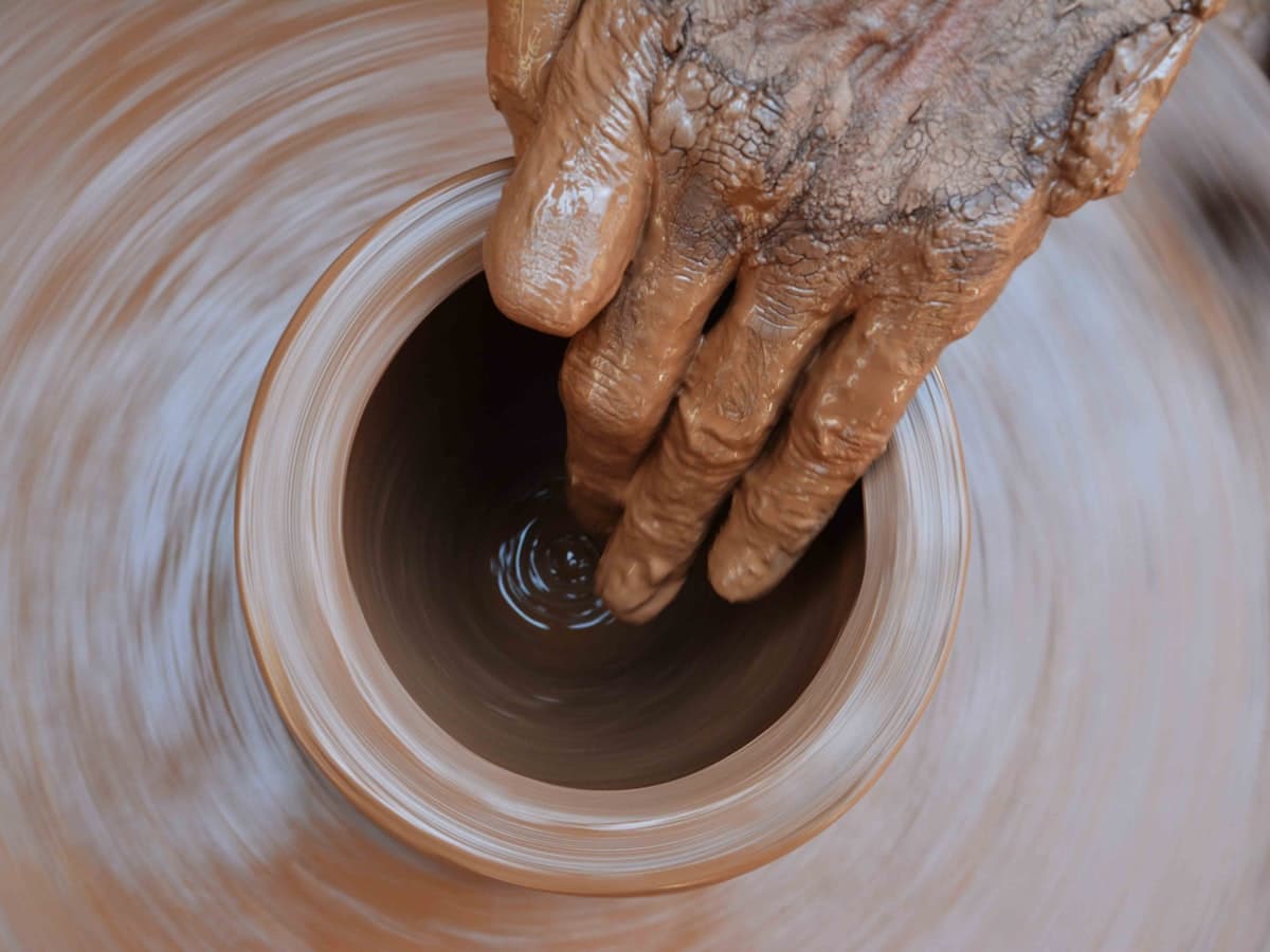 A potter's hands draw up a wet clay pot on a spinning wheel, the traditional craft that Likir village still keeps alive.