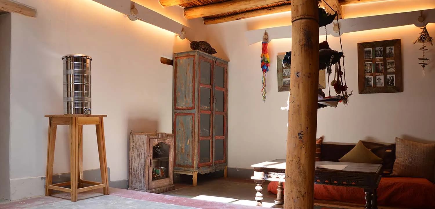 Interior lounge at Nimmu House with a carved wooden pillar, low seating and traditional Ladakhi textiles