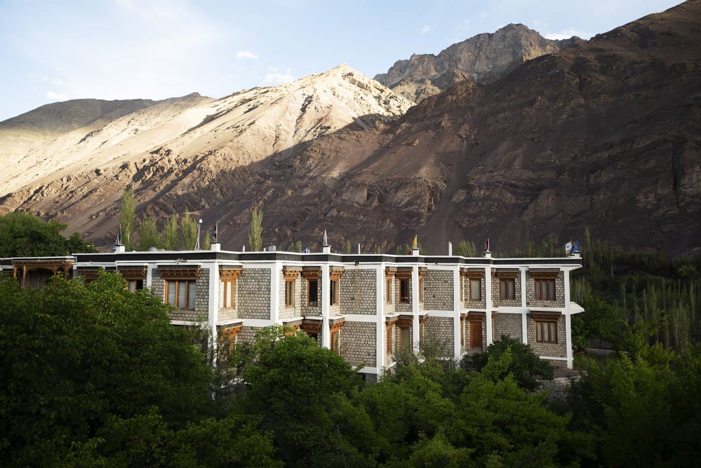 The Apricot Tree hotel's stone-and-timber Ladakhi building set among green trees below bare desert mountains near Nurla, Sham valley