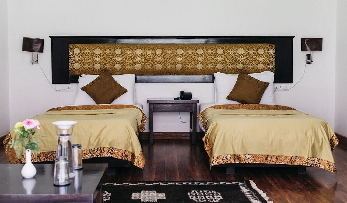 A twin guest room at The Apricot Tree with Ladakhi-heritage decor, wood panelling and a brass tray on the table