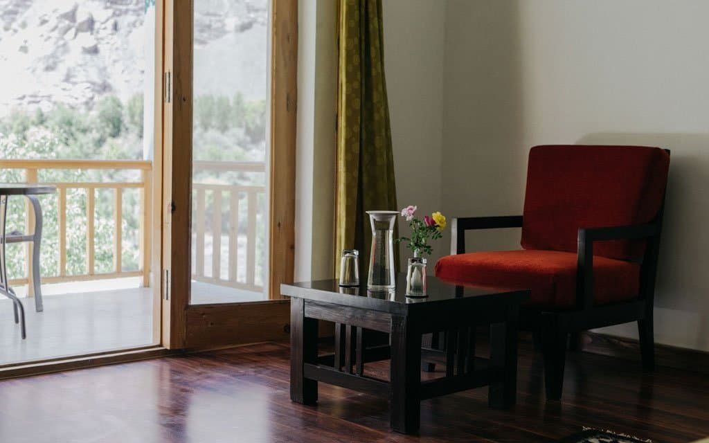 A guest room at The Apricot Tree with a red armchair by the balcony doors, wooden floor and river-valley view