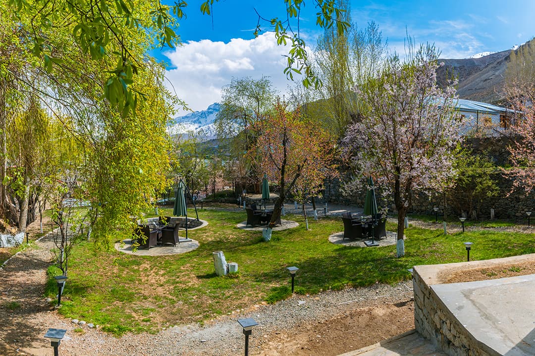 The landscaped lawn garden at Hotel The Kargil, with blossoming trees and the bare mountains of Kargil town behind