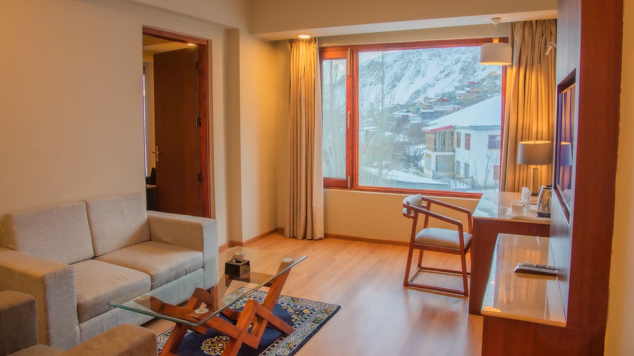 A guest room at Hotel The Kargil with a sofa, work desk and a large window framing the Himalayan foothills