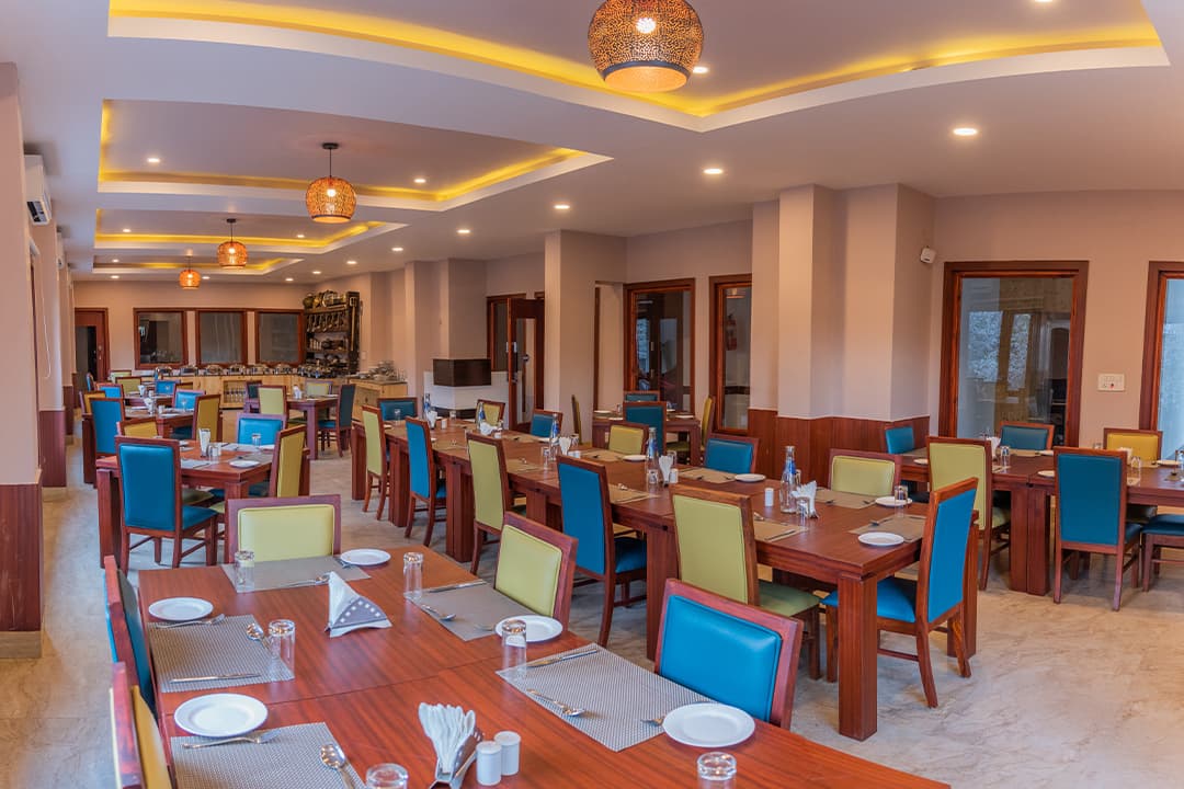 The restaurant at Hotel The Kargil, a bright dining room with brightly coloured chairs and set tables
