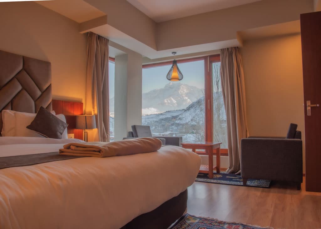 A superior suite at Hotel The Kargil with a made bed, wood panelling and a balcony opening to a mountain view