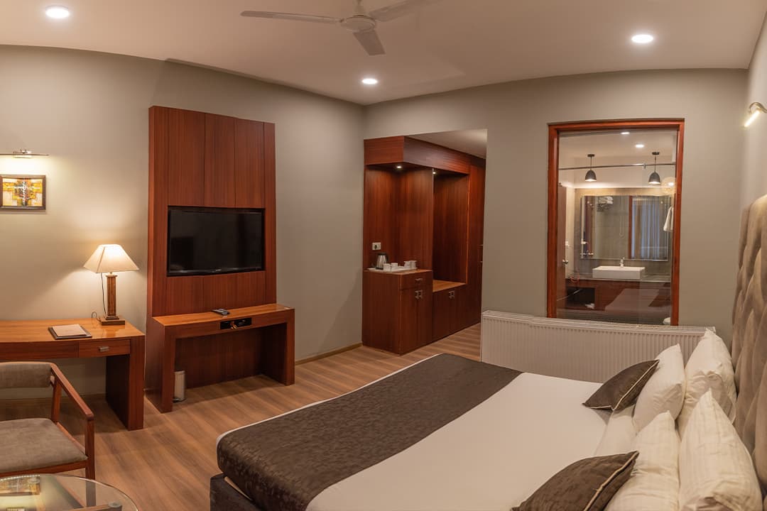 A premium double room at Hotel The Kargil with a patterned headboard, work desk, flat-screen TV and warm interior tones