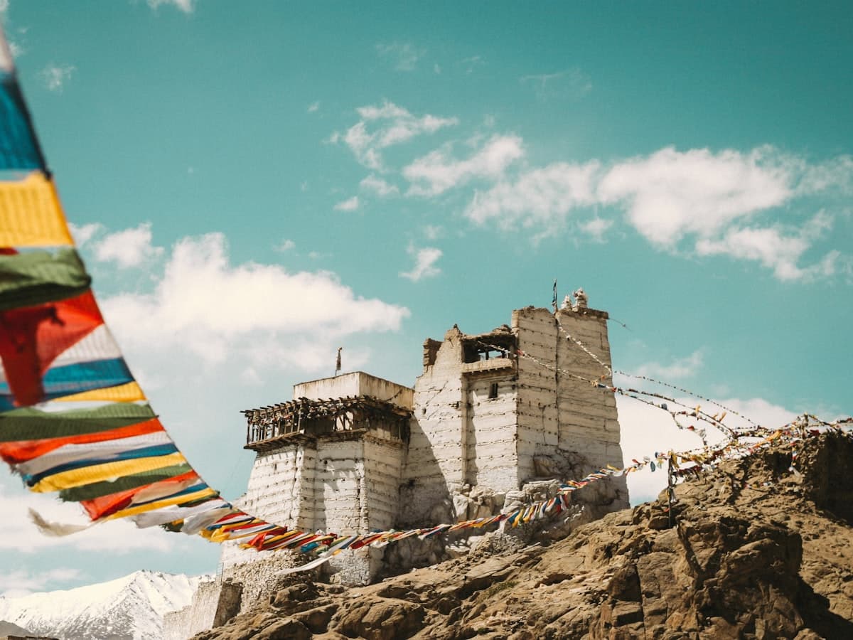 An ancient whitewashed monastery clings to a rocky spur, its ridgeline strung with weathered prayer flags above the valley.